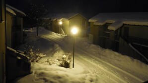 A snowy residential street at night with houses on both sides and a street lamp in the foreground.