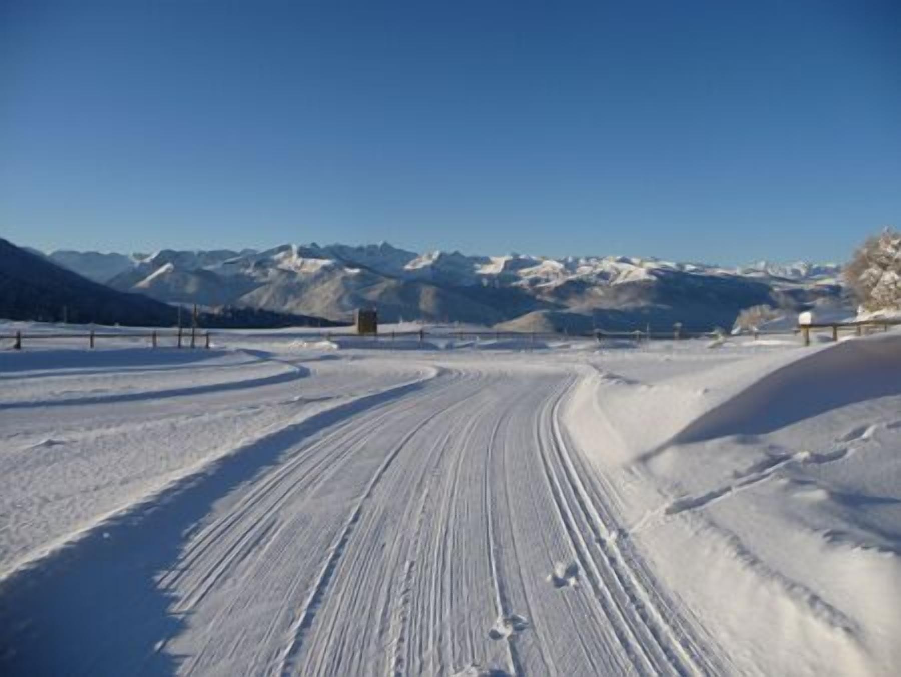 Een besneeuwde weg met een vangrail en een klein gebouw in de verte, omringd door bergen.