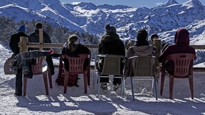 A group of people seated on plastic chairs facing a snowy mountain backdrop.