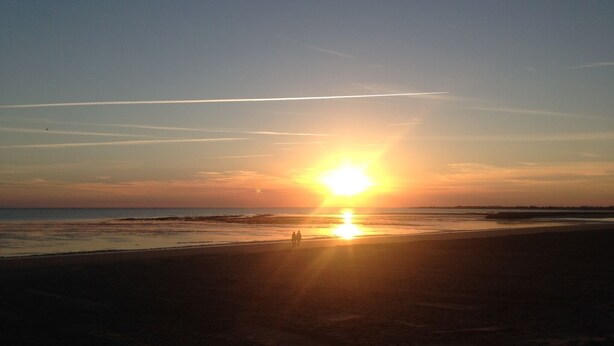 Een strand bij zonsondergang met een heldere lucht en een zichtbare vliegtuigspoor.