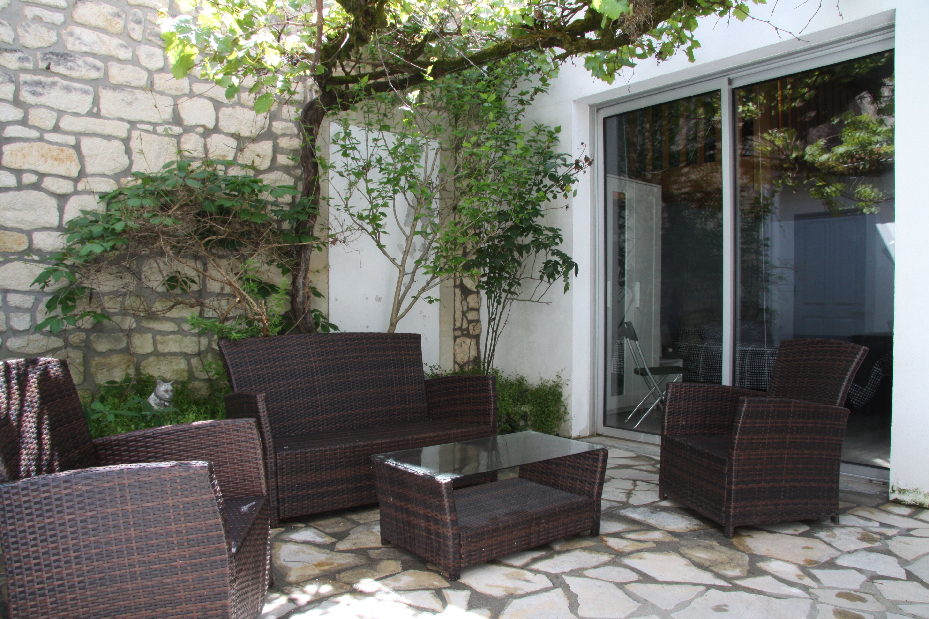 Un patio con mobiliario de mimbre, una mesa de vidrio y suelo de piedra.