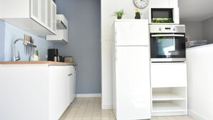 Een kleine keuken met witte kastjes, een ingebouwde oven en een klok aan de muur.