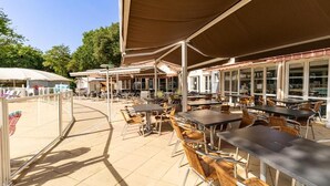 Un espace extérieur aménagé en terrasse, avec des tables et des chaises, protégé par de grands parasols et entouré de baies vitrées.