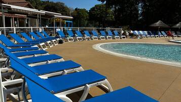 Un espace aménagé au bord de la piscine, avec des chaises longues bleues disposées en rangées, une piscine à l’eau claire et, au fond, un bâtiment doté d’un toit recouvert de tuiles.