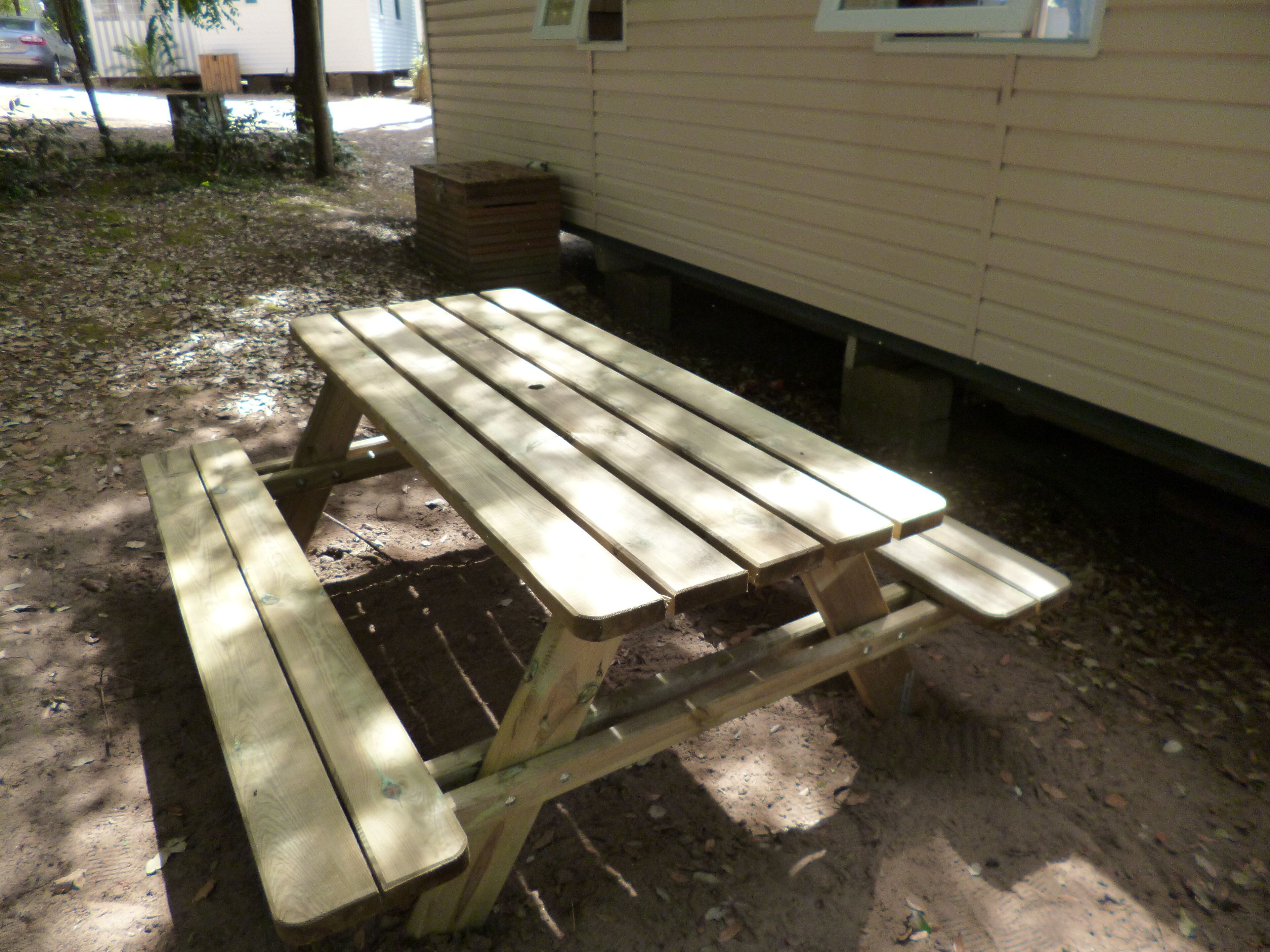 Une table de pique-nique en bois, avec des bancs, placée à l’extérieur, près d’un bâtiment.