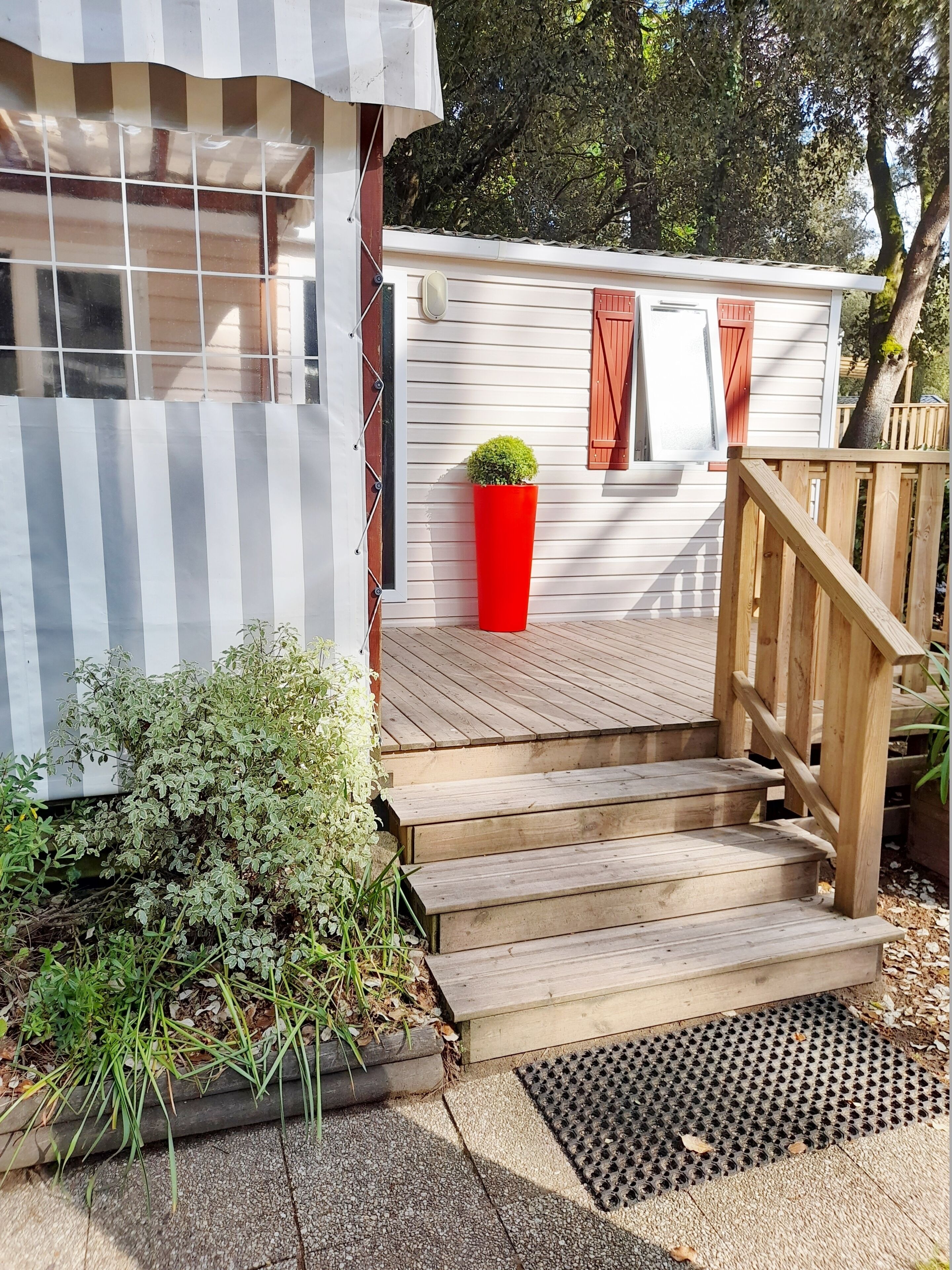 A wooden deck with steps leading to a white building with striped awning and red shutters.