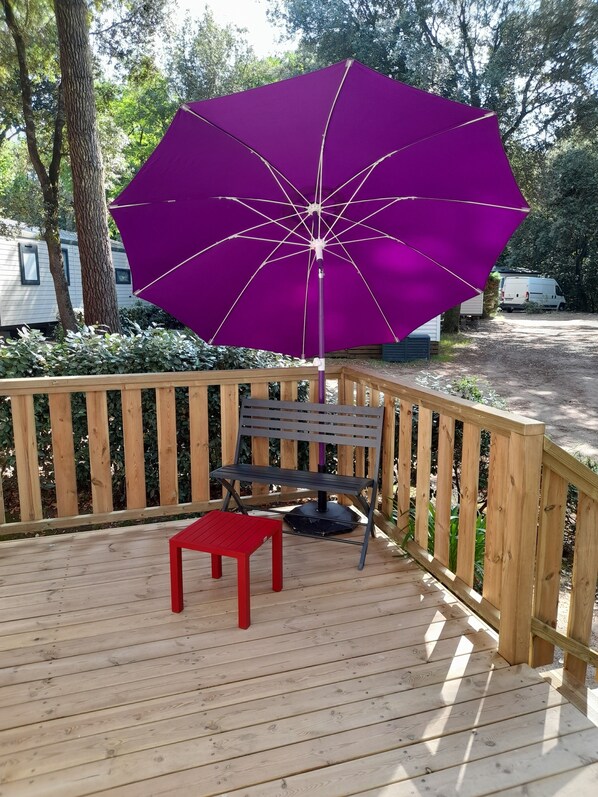Une terrasse en bois avec un parasol violet, une table rouge et un banc.