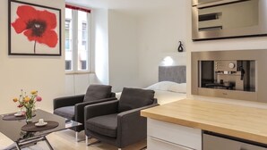 A modern hotel room with a bed, a seating area with two chairs, a small table with a vase of flowers, and a kitchenette with a stove and oven. - Studio charm in the heart of Old Nice (Nice)
