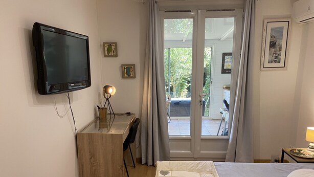 A bedroom with a bed, a desk with a computer, a TV, and a view of the outdoors. - House with small garden in a quiet area 3 minutes from the town center (La Rochelle)