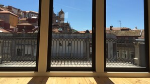 Vista a través de tres ventanas de un edificio con balcón, que presenta una barandilla de hierro forjado y un cielo azul despejado.