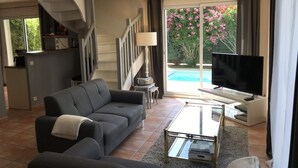 A living room with a sofa, coffee table, TV, and a staircase leading to a balcony with a pool view.