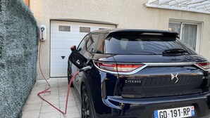 A black SUV parked outside a house with a charging cable connected to a wall-mounted charging station.