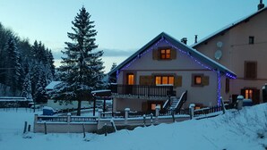 Una casa cubierta de nieve con un balcón, rodeada de nieve y árboles.