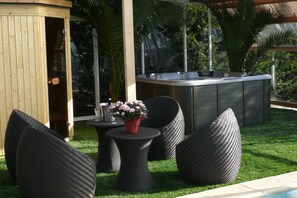 An outdoor seating area with wicker furniture, a small round table with a potted plant, and a built-in hot tub.