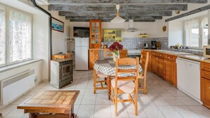 A kitchen with wooden cabinets, a dining table with chairs, a refrigerator, a stove, and a window with curtains.