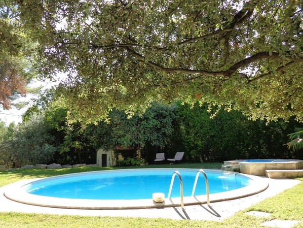 A circular swimming pool with a metal ladder, surrounded by a grassy area and trees.