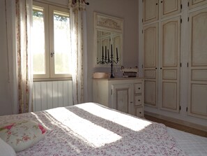 Ein Schlafzimmer mit einem Bett, einem Schminktisch, einem Spiegel und einem Fenster mit Vorhängen.