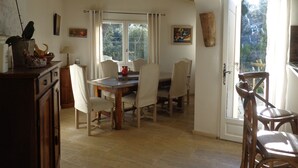 A dining area with a wooden table and chairs, a window with curtains, and a view of greenery outside. - Typical and luxurious house in the very heart of provence with swimming pool . (Vaucluse)