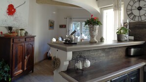 A kitchen with a wooden cabinet, a white countertop, a large clock, and a window with curtains. - Typical and luxurious house in the very heart of provence with swimming pool . (Vaucluse)