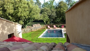 Un jardin avec une piscine, des chaises longues rouges et un mur en pierre.