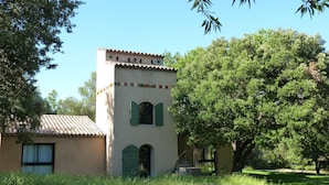 Un bâtiment doté d’un toit en tuiles et de fenêtres en arc de cercle, entouré d’une végétation luxuriante et d’arbres.