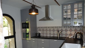 Une cuisine moderne avec des armoires grises, un four encastré, un four à micro-ondes, un luminaire suspendu et un pare-feu en carrelage.