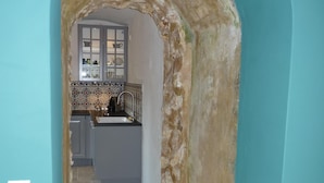 Un couloir étroit, surmonté d’une arche en pierre, mène à une cuisine.