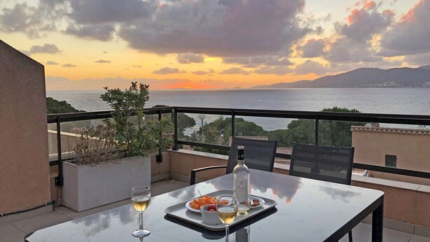 Un balcon avec une table dressée pour deux personnes, agrémenté d’une bouteille de vin et d’une assiette de fruits.