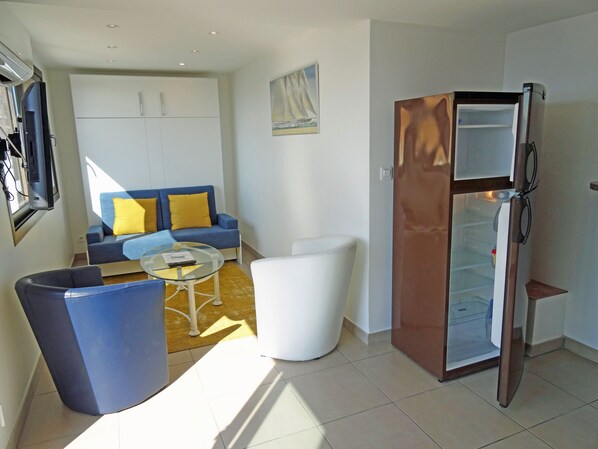 Un espacio habitable compacto con sofá, mesa de centro, silla blanca y refrigerador.