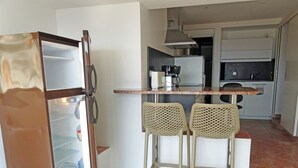 Une cuisine compacte équipée d’un réfrigérateur, d’une machine à café et de deux tabourets de bar.