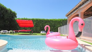 Een zwembad met een roze flamingo drijver, een rode parasol en ligbedden.