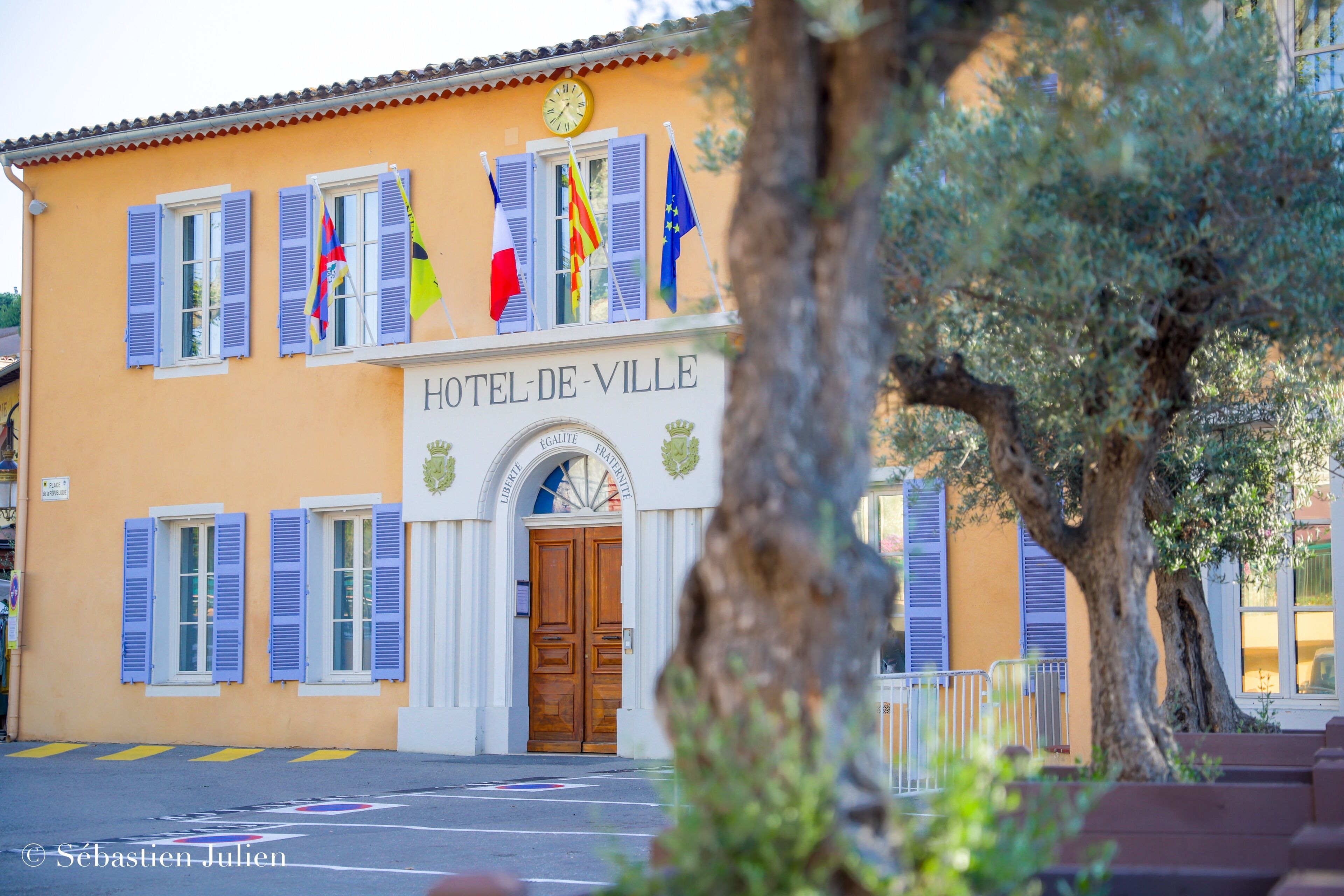 A building with the sign "HOTEL-DE-VILLE" and multiple flags, including the French flag.