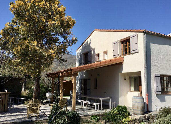 A two-story building with a pergola, outdoor seating, and a barbecue grill.