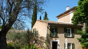 A traditional building with a tiled roof, green shutters, and a stone bench in the foreground.