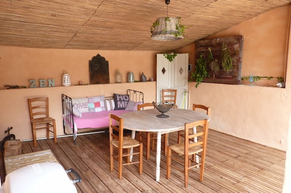 A cozy room with a wooden floor, a round table with chairs, a sofa with cushions, a hanging plant, and a wall with decorative items.