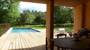 A wooden deck with a hot tub, surrounded by a metal fence, and overlooking a grassy area with trees.