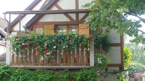 Une maison traditionnelle à colombages, dotée d’un balcon recouvert de plantes grimpantes en fleurs.