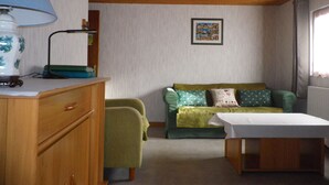 Une pièce avec un plafond en bois, un canapé vert, une table blanche et une lampe posée sur une commode en bois.