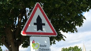 Un panneau de signalisation indiquant la direction de la Route des Châteaux d’Alsace, avec un panneau d’avertissement triangulaire placé au-dessus.