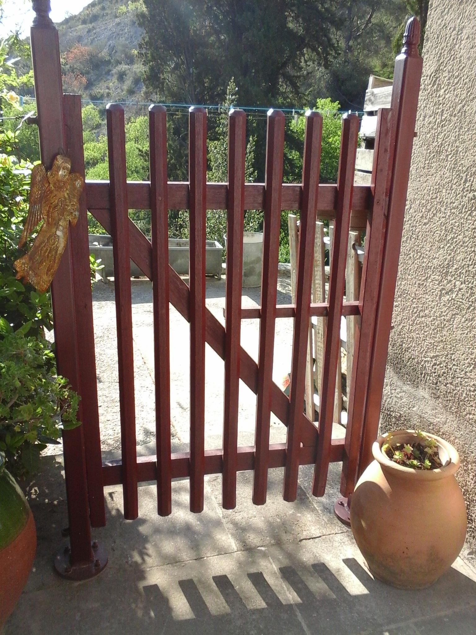 A gated entrance with a wooden gate, a potted plant, and a decorative angel figure.