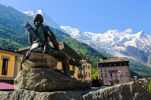 A statue of a seated figure on a rock with a mountainous backdrop and buildings in the foreground.