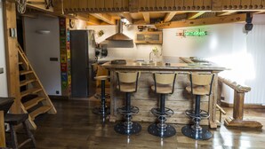 Una cocina rústica con detalles de madera, una zona de bar con taburetes, un letrero de Heineken y una escalera.