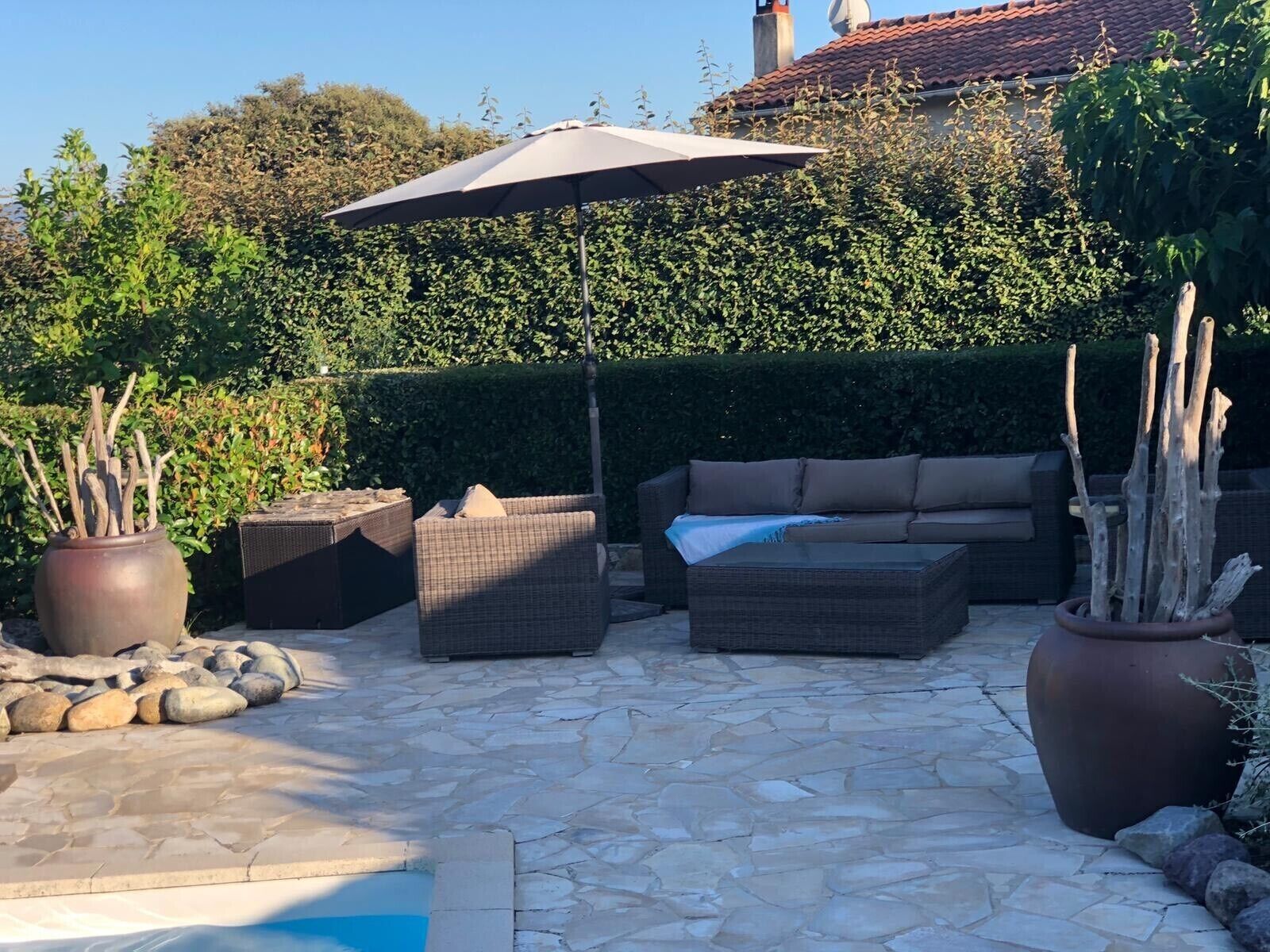 An outdoor patio with stone flooring, wicker furniture, and potted plants.