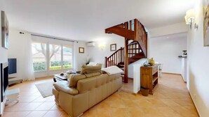 A spacious living area with a sofa, a wooden staircase, and a TV. - Air-conditioned villa with private pool and jacuzzi, in a quiet location close to beaches. (Appietto)