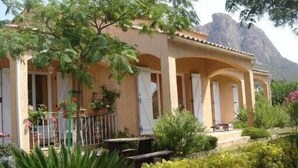 A two-story building with a balcony, surrounded by lush greenery and a mountainous backdrop. - Air-conditioned villa with private pool and jacuzzi, in a quiet location close to beaches. (Appietto)