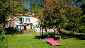 Una casa con un tobogán rojo en el jardín, rodeada de árboles y un cielo azul despejado.