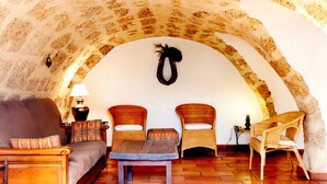 Un salón acogedor con un arco de piedra, un sofá, dos sillones de mimbre, una mesita y un tapiz decorativo.