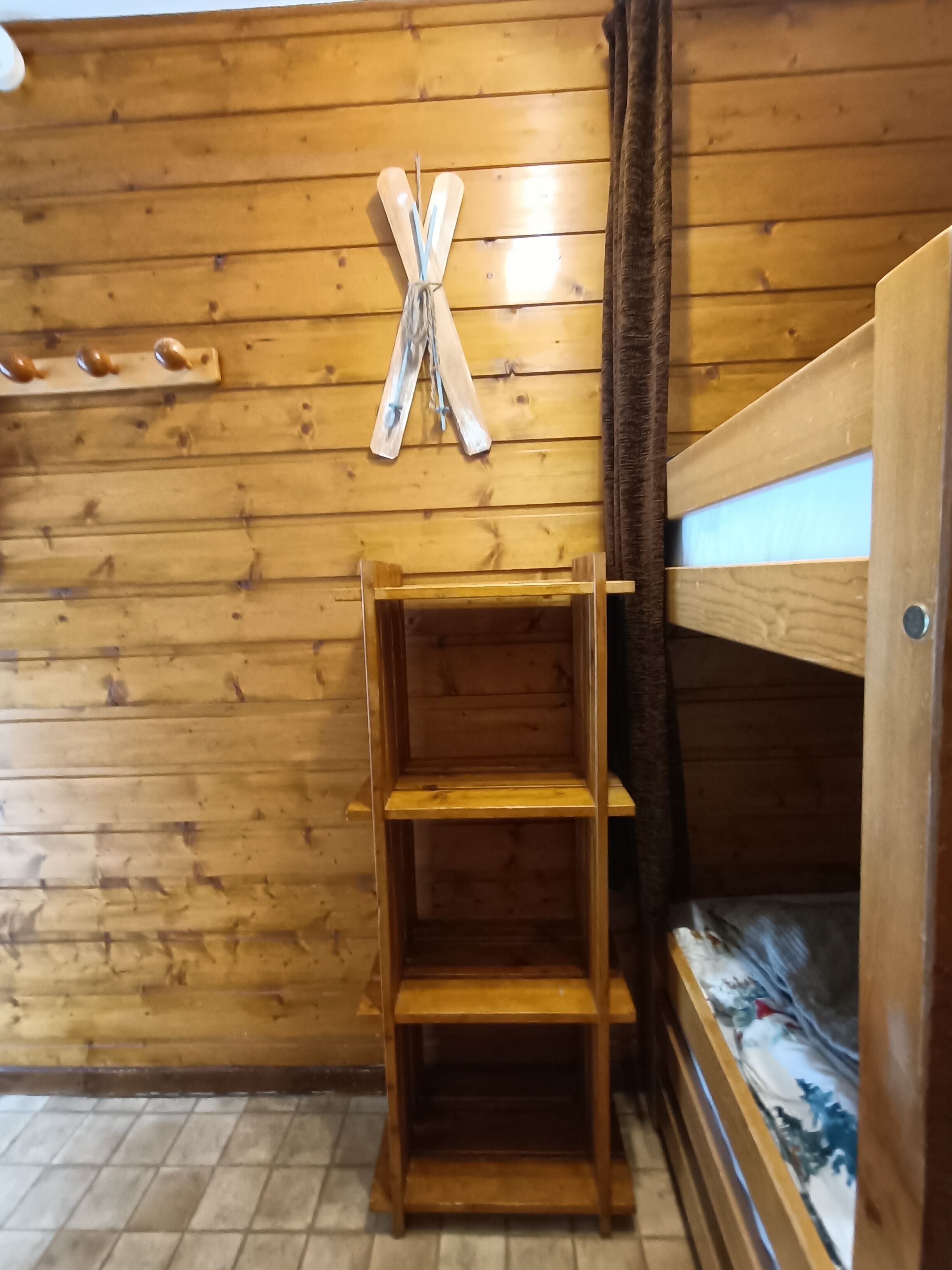 Una stanza in legno con un letto a castello, una scaffalatura in legno e una X di legno fissata alla parete.