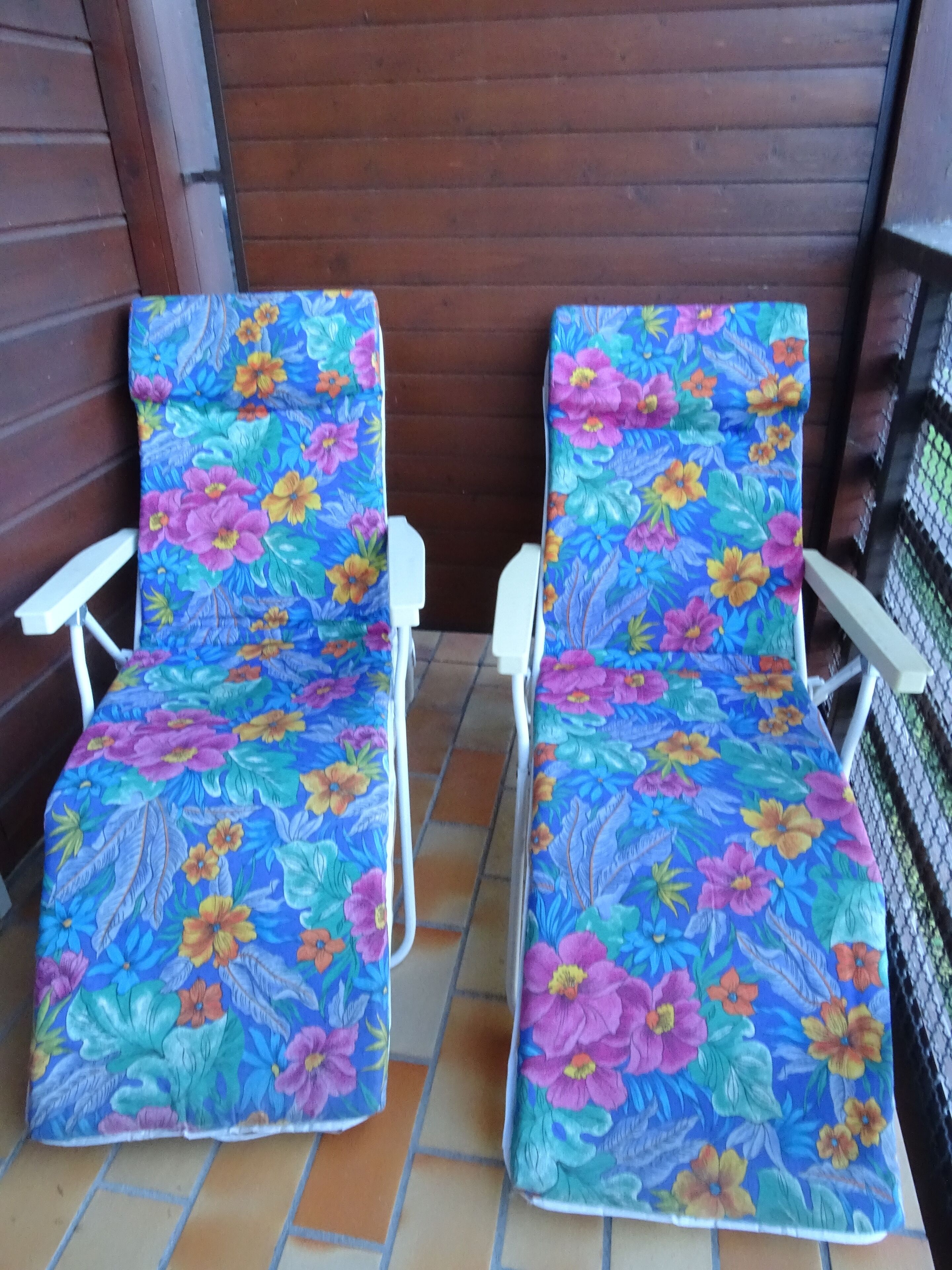 Dos sillones con tapicería floral sobre piso de baldosas, ubicados en una terraza de madera con baranda metálica.