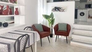 A modern kitchen with a washing machine, a dining area with a table and chairs, and a living area with two armchairs and a potted plant. - Gîte le chat vert. The most beautiful villages in France  (Robion)